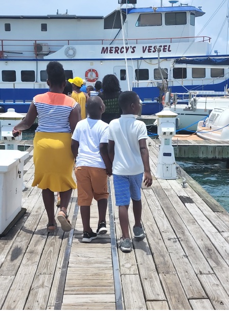 A family photographed from behind, walking along a wooden dock toward the mission vessel Mercy.