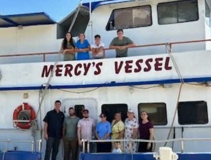 About ten volunteers standing together on the deck of the vessel Mercy.